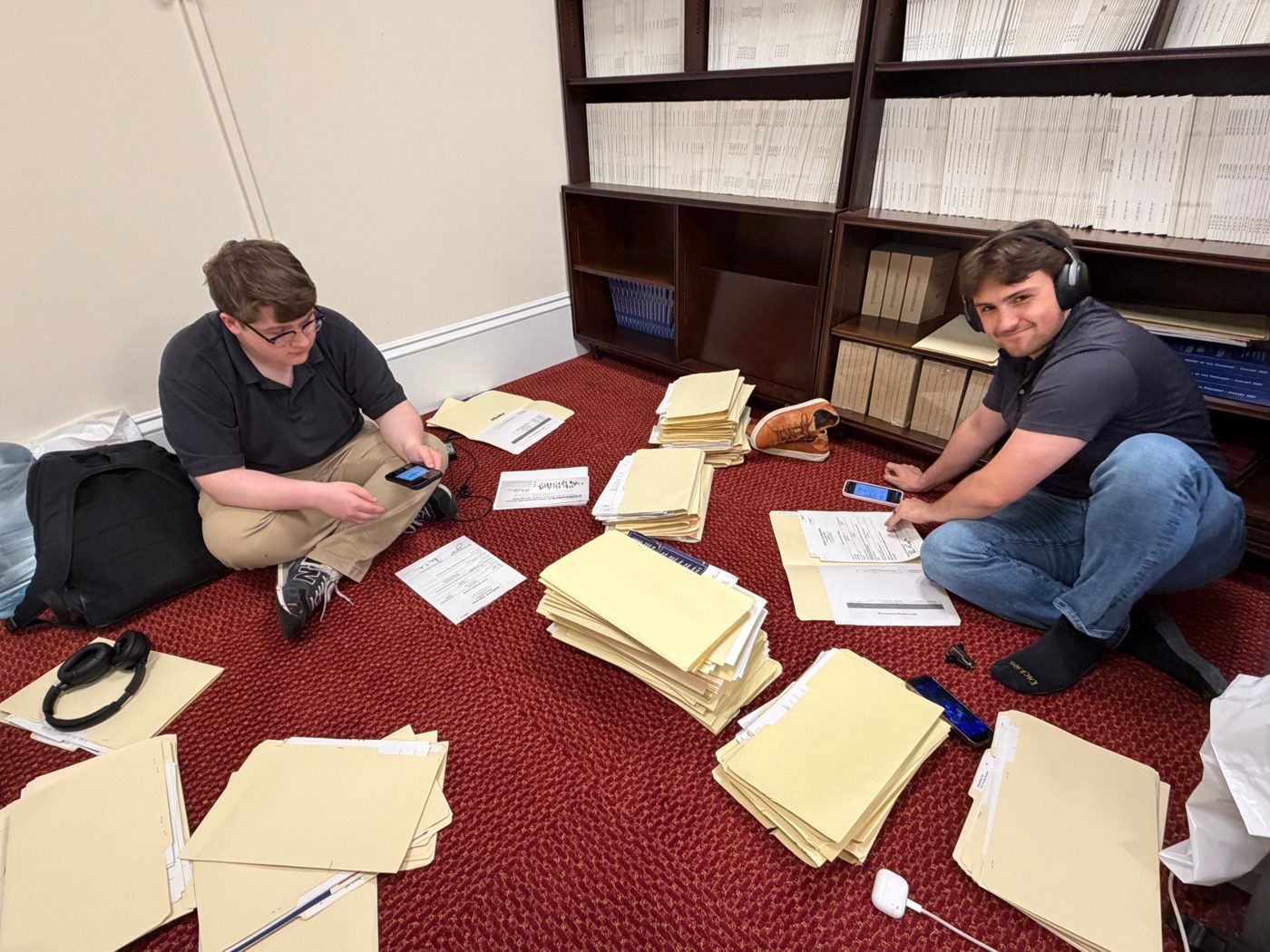Two students sorting stacks of archival folders on the floor